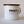 Load image into Gallery viewer, A side view of Fault Line's white enamel mug. The mug has a black lip. The front of the mug has a black Fault line logo on it.