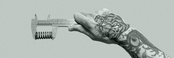 A tattooed male hand measures a clutch spring with Vernier Calipers