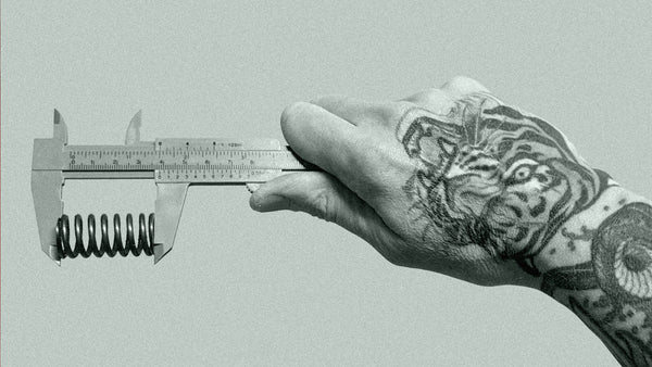 A tattooed male hand measures a clutch spring with Vernier Calipers