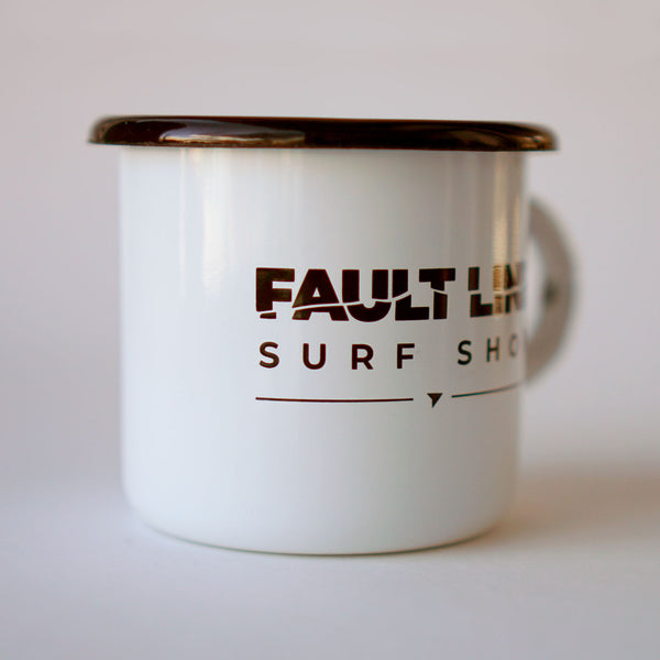 A side view of Fault Line's white enamel mug. The mug has a black lip. The front of the mug has a black Fault line logo on it.