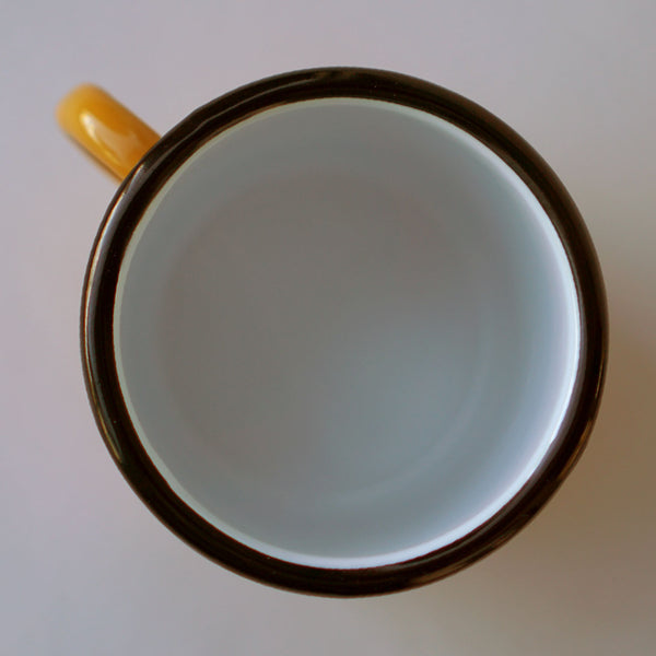 An overhead view of Fault Line's yellow enamel mug. The lip of the mug is black, the inside is white.