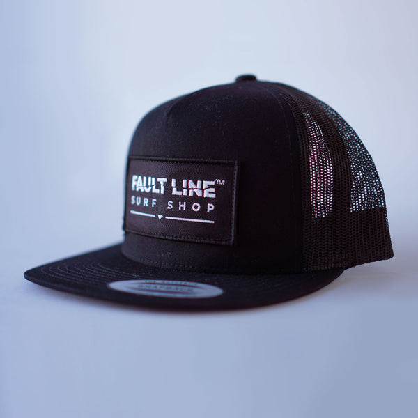 A three-quarter view of Fault Line's black snapback trucker cap. The front of the cap has an embroidered patch with the logo on it.