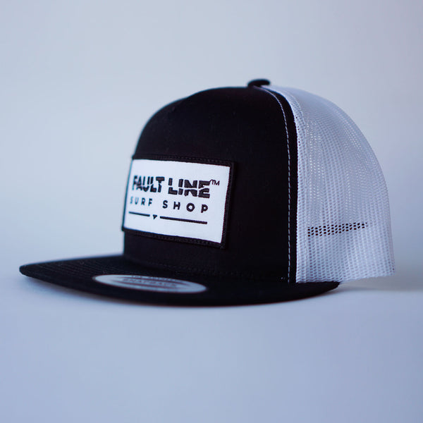 A three-quarter view of Fault Line's black & white snapback trucker cap. The front of the cap has an embroidered patch with the logo on it.