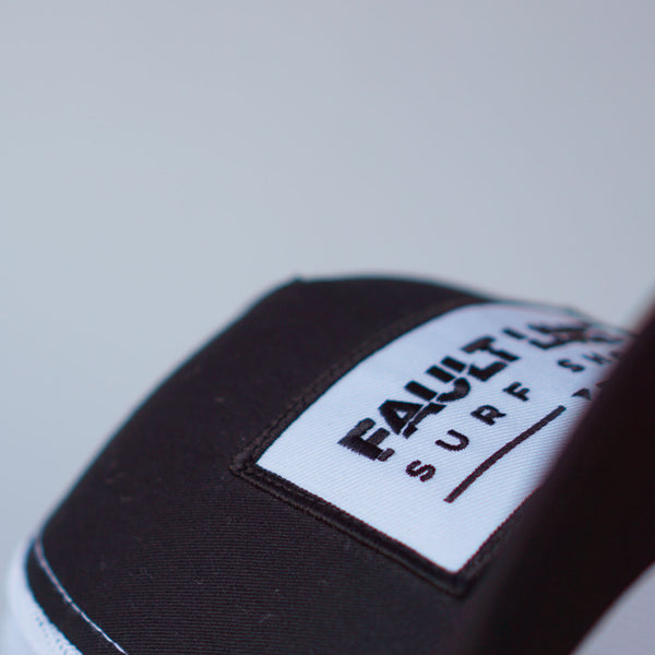 Another close-up of Fault Line's black & white snapback trucker cap. The front of the cap has an embroidered patch with the logo on it.